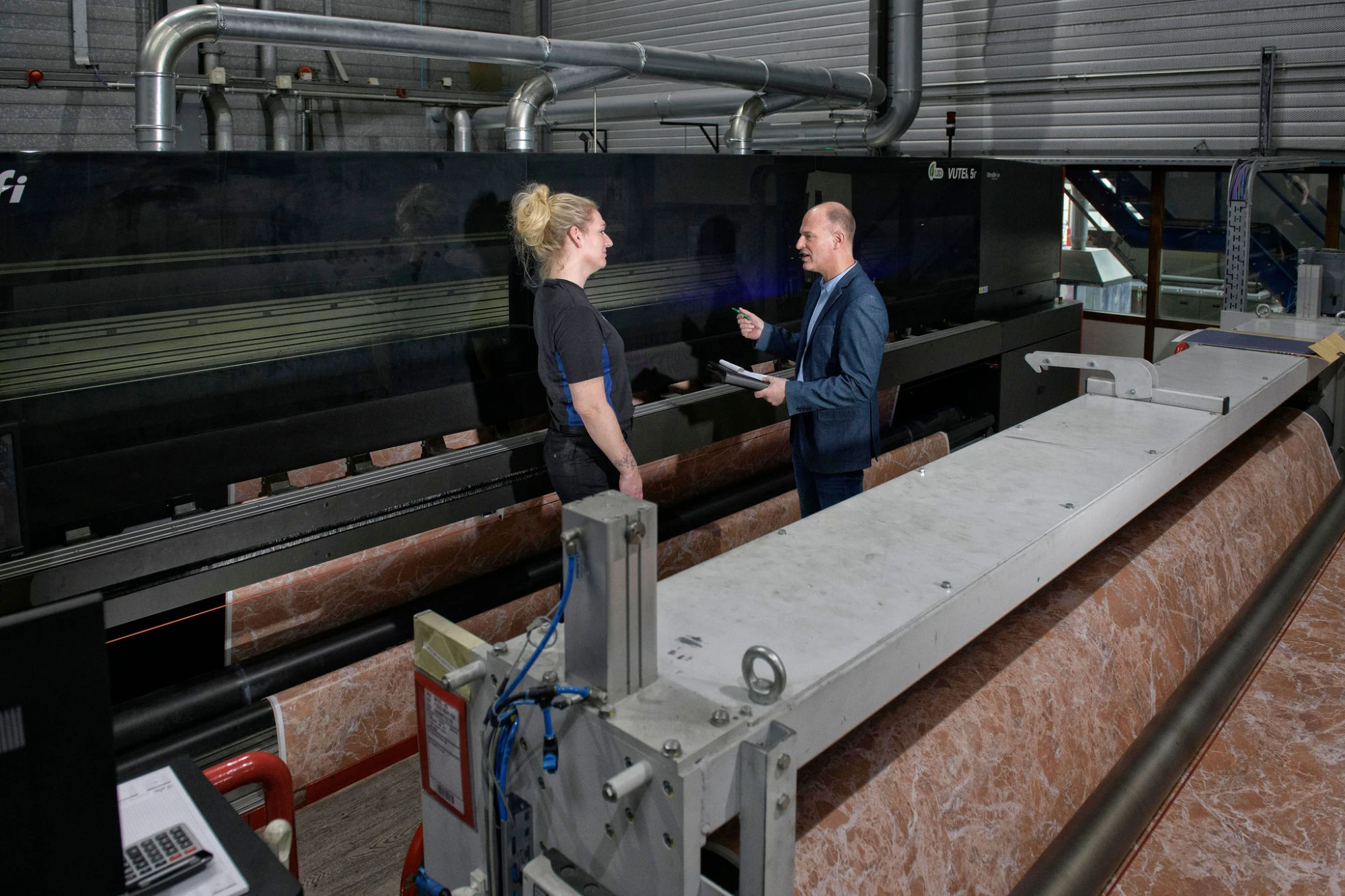 Man en vroue in een fabriekshal. Man voert een RI&E uit en geeft advies